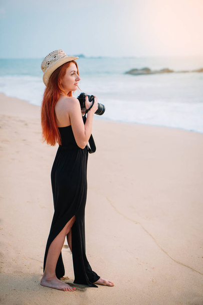 young woman photographer stands on the beach with a camera in hands - 写真・画像