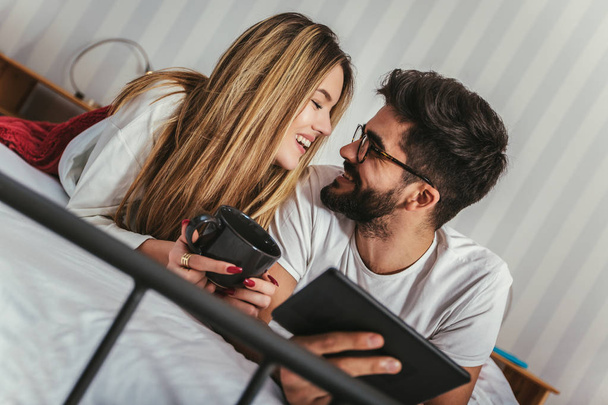 Young attractive couple in bed, using digital tablet. - Foto, Imagen