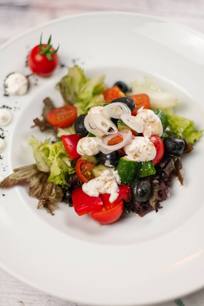Крупный план греческого салата с помидорами черри, оливками, нарезанными огурцами, сладким перцем и сыром фета на белой тарелке
 - Фото, изображение