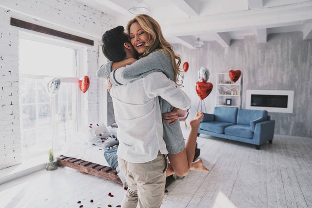 Totally in love beautiful couple embracing in bedroom full of balloons and rose petals, celebrating valentines day and engagement - Фото, изображение
