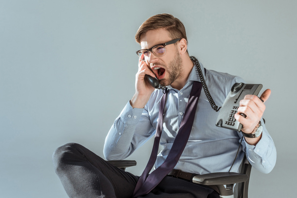 Young annoyed businessman yelling while talking on phone isolated on grey - Photo, Image