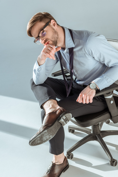 Young thoughtful businessman sitting on chair with hand on chin - Photo, Image