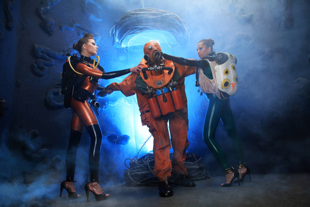 homem vestido com traje retro mergulho histórico, posando com mulheres amantes em um látex borracha fetiche catsuits e saltos altos
 - Foto, Imagem