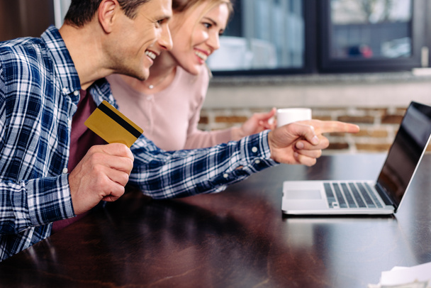 happy couple with credit card and cup of coffee looking at laptop screen at home - Fotoğraf, Görsel