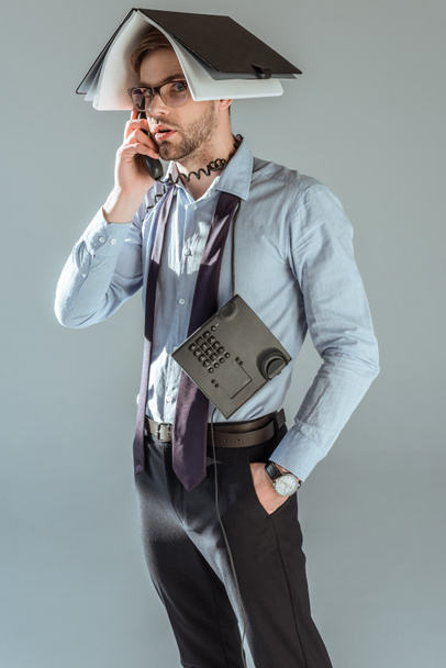 Confused businessman holding notebook on his head while talking on phone isolated on grey - Photo, Image