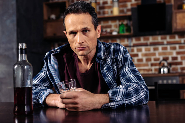 mężczyzna siedzący przy stole z butelkę i kieliszek alkoholu w domu - Zdjęcie, obraz