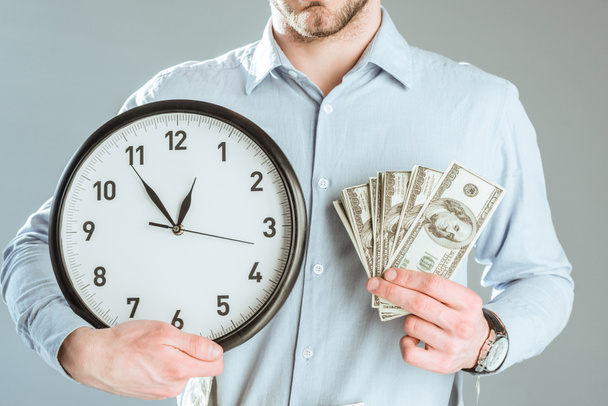Close-up view of businessman showing money and clock isolated on grey - 写真・画像
