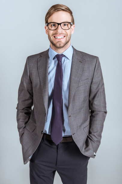 Молодий усміхнений бізнесмен з руками в кишенях ізольовані на сірому
 - Фото, зображення