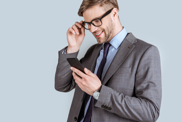 Young businessman looking at smartphone screen isolated on grey - Photo, Image