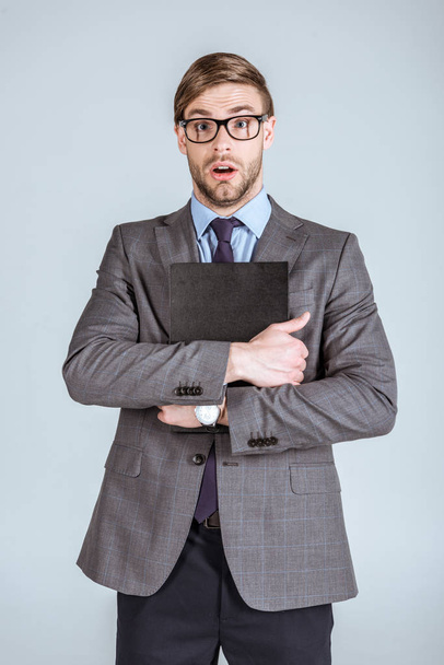Молодий здивований бізнесмен тримає блокнот ізольовані на сірому - Фото, зображення