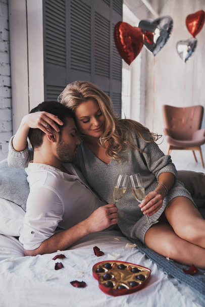 Beautiful couple with champagne glasses celebrating Valentines Day at home on bed - Foto, imagen