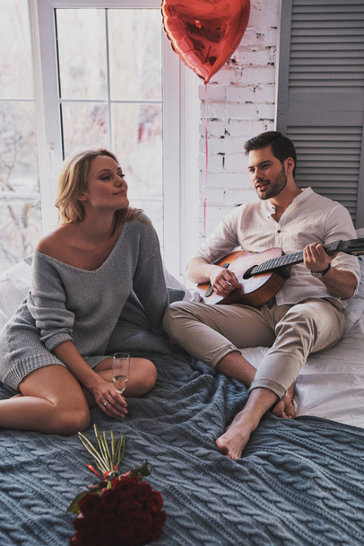 man playing acoustic guitar to beautiful girlfriend while celebrating Valentines Day at home - 写真・画像