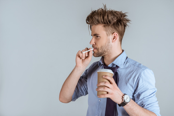 Unavený podnikatel drží pohárek a kouření cigaret izolované Grey  - Fotografie, Obrázek