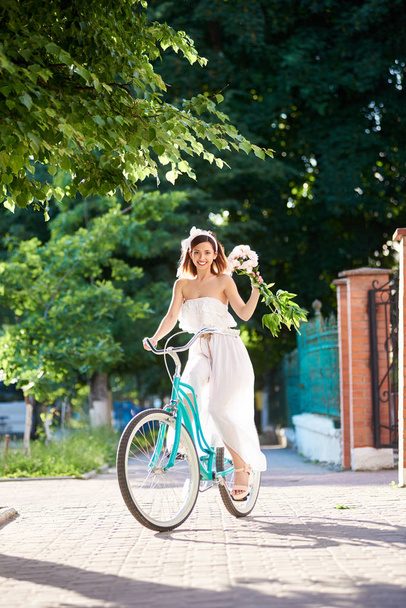 Frau mit Strauß von Pfingstrosen in der Hand fährt Oldtimer-Fahrrad entlang der Stadtstraße  - Foto, Bild