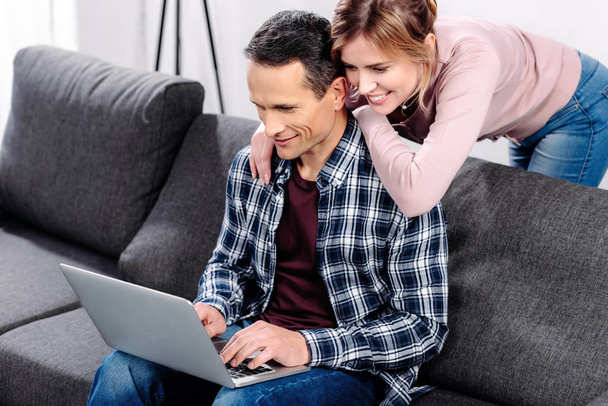 portrait de couple souriant avec ordinateur portable sur canapé à la maison
 - Photo, image