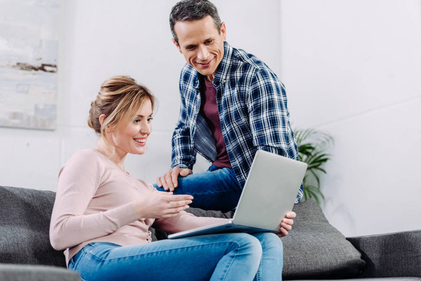 smiling couple using laptop on sofa at home - Photo, Image
