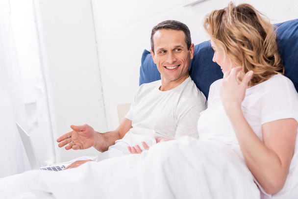 smiling couple with laptop in bed at home - Photo, Image