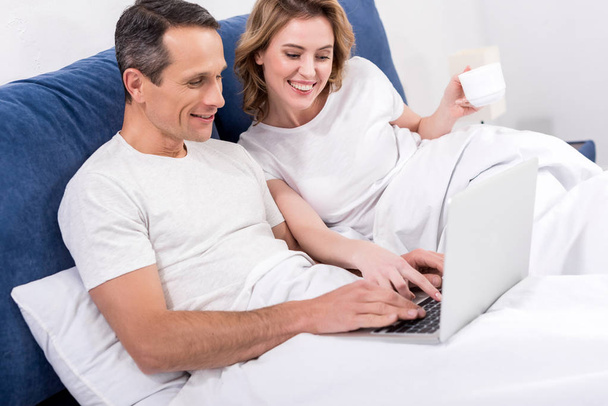 portrait of smiling couple with laptop in bed at home - Фото, зображення