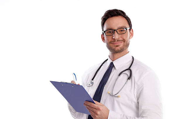 slimme knappe bebaarde arts in glazen met stethoscoop geïsoleerd op een witte achtergrond. Man uit ziekenhuis met een Klembord is klaar om te schrijven iets neer - Foto, afbeelding