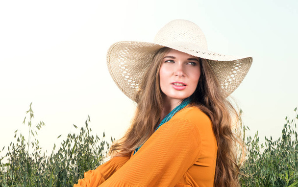 Closeup portret van de jonge vrouw zitten in een veld. Strooien hoed en rode jurk - Foto, afbeelding