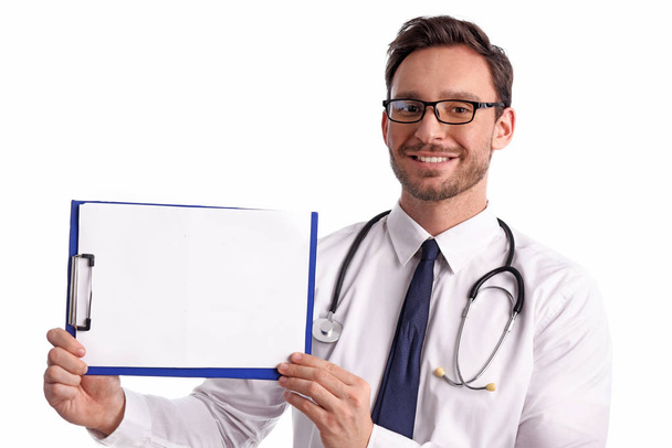 Smart przystojny Brodaty lekarz medycyny w okularach z stetoskop izolowana na białym tle. Człowiek ze szpitala z Schowka jest gotów napisać coś w dół - Zdjęcie, obraz