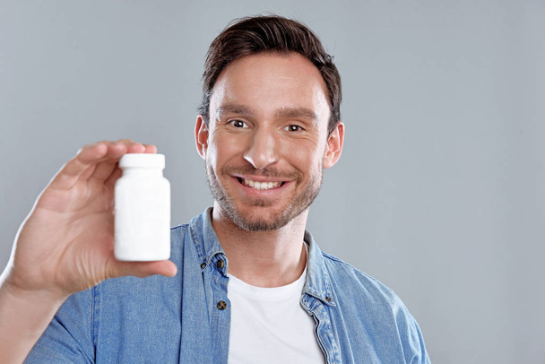 Handsome bearded man isolated on a white background with a bottle of pills. He trusts this medicine and he is happy because he wants to be healthy again. - Foto, Bild