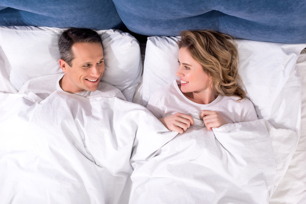 overhead view of smiling wife and husband lying in bed at home - Foto, Imagen