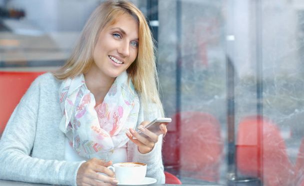 Charming happy female reading news on cell telephone during breakfast in cafe - Photo, Image