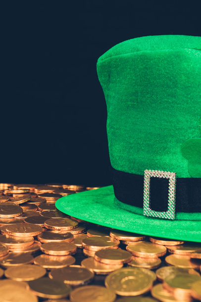 groene hoed op de glimmende gouden munten geïsoleerd op zwart, st patricks dag concept - Foto, afbeelding