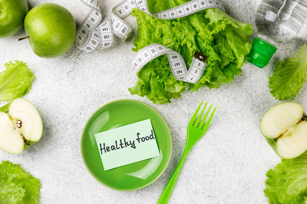Healthy eating. Green apple, lettuce salad, water bottle, measuring tape. Dieting, slimming, weight loss and meal planning concept - Photo, Image