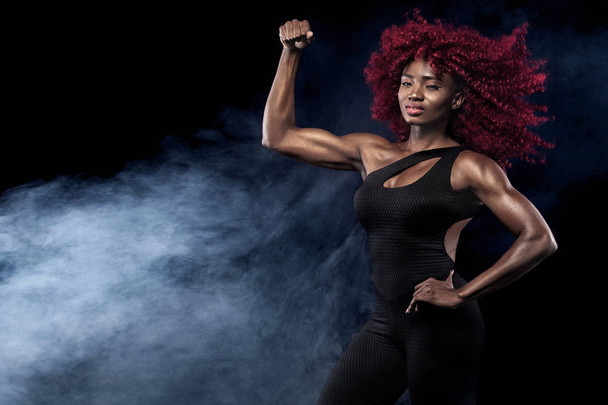 Sporty beautiful afro-american model, woman in sportwear makes fitness exercising at black background to stay fit - 写真・画像