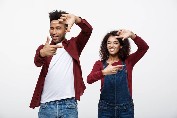 Boldog fiatal African American pár látszó átmenő egy ujj keret, és mosolyogva, miközben állandó elszigetelt fehér. - Fotó, kép