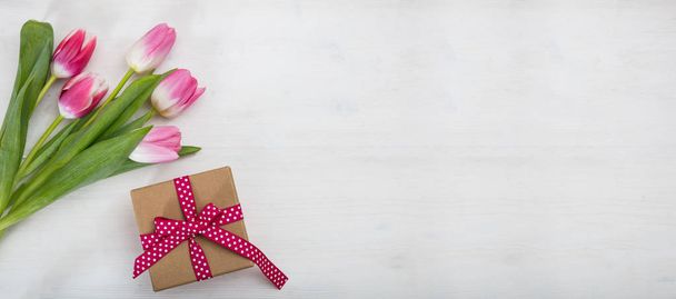 Naistenpäivä. Vaaleanpunainen tulppaanit ja lahja valkoisella taustalla, banneri, ylhäältä, copyspace
 - Valokuva, kuva