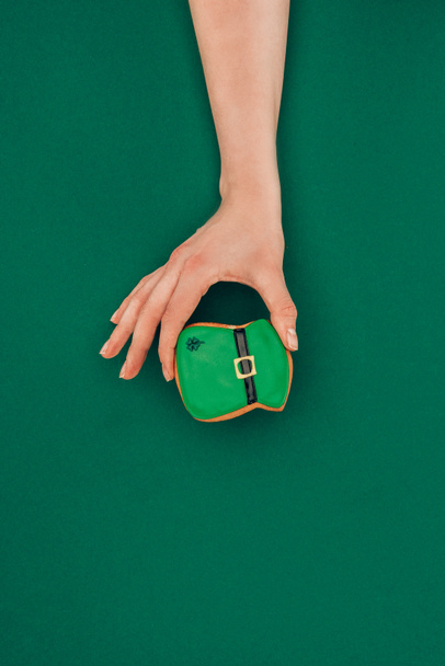 cropped image of woman holding cookie in shape of hat isolated on green, st patricks day concept - Photo, Image