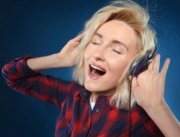 Felice ragazza bionda è felice di ascoltare la sua musica preferita in cuffia e cantare insieme alle sue canzoni preferite isolate su uno sfondo blu
 - Foto, immagini