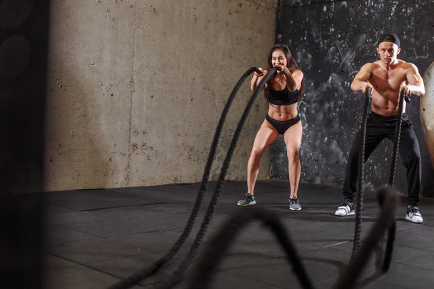 Woman and man couple training together doing battling rope workout - Foto, afbeelding