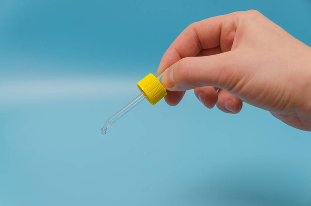 on a blue background, male hand, falling drops from the pipette - Fotó, kép