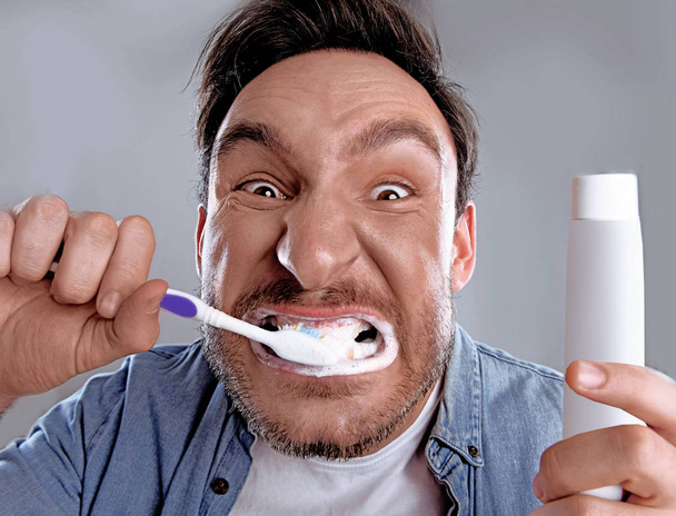 Yakışıklı komik sakallı adam beyaz gömlekli mi saplantı onun diş sağlığı hakkında o onları zor bir diş macunu ve diş fırçası ile temizlenir ve şimdi mutlu olduğunu - Fotoğraf, Görsel