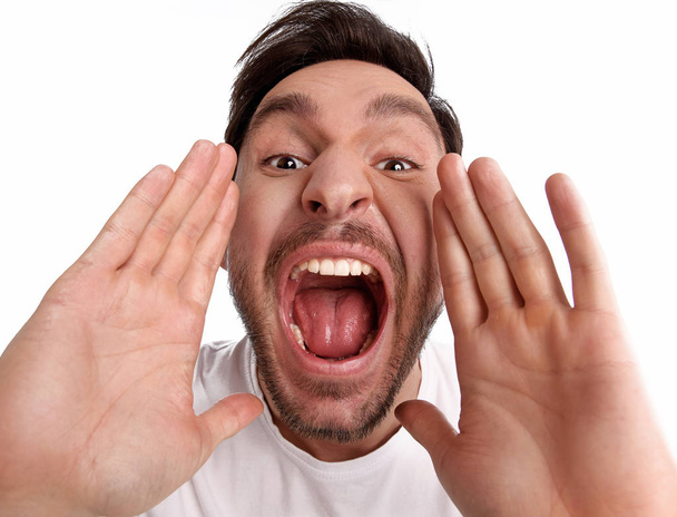 Knappe bebaarde grappige man is schreeuwen met zijn mond wijd open is geïsoleerd op een witte achtergrond met zijn handen omhoog - Foto, afbeelding