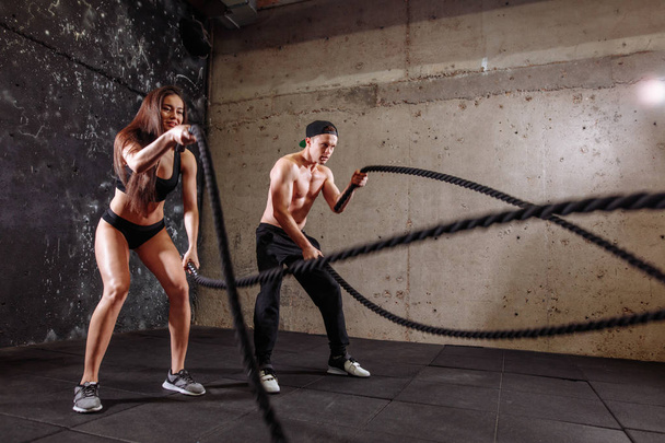Woman and man couple training together doing battling rope workout - Foto, imagen