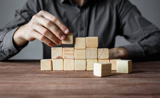 Closeup of businessman making a pyramid with empty wooden cubes. Concept of business hierarchy and business strategy. - 写真・画像