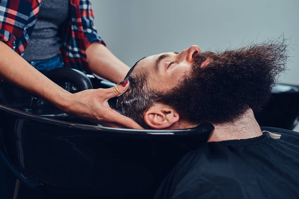 Professional hairdresser washes client head in a black trendy washbasin. Barbershop - Foto, Imagem