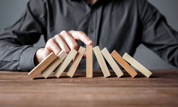 Businessman stopping domino effect with his finger. Security and insurance concept. - Fotoğraf, Görsel