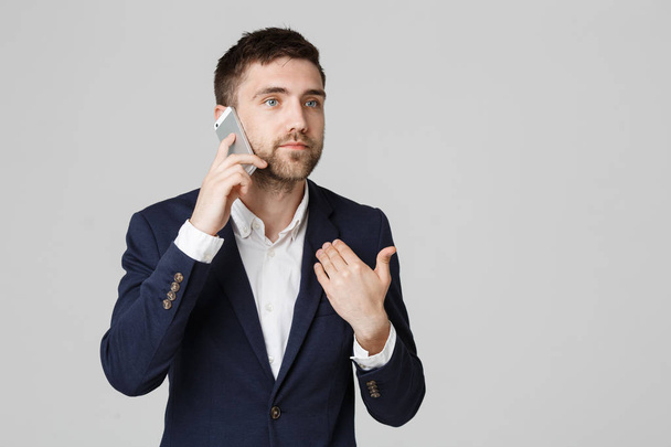Obchodní koncept - portrét mladý pohledný naštvaný obchodní muž v obleku mluví v pohledu kamery telefonu. Bílé pozadí. - Fotografie, Obrázek