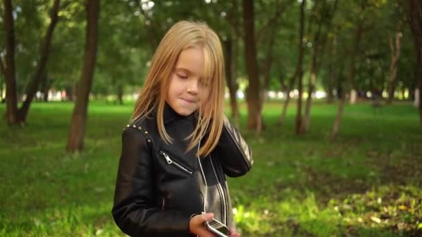 Girl in a leather jacket listening to music in park - Кадры, видео