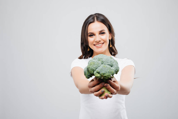 Portret van een mooie lachende vrouw met broccoli, geïsoleerd op witte achtergrond - Foto, afbeelding