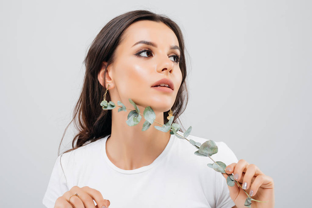 Beauty portrait of a pretty woman with brunette hair posing with eucalyptus leaves isolated over white background - Fotografie, Obrázek