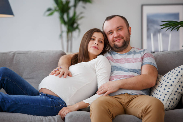 Picture of happy future parents sitting on gray sofa - Photo, image