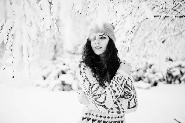 Cute curly girl in sweater and headwear at snowy forest park at  - Foto, immagini