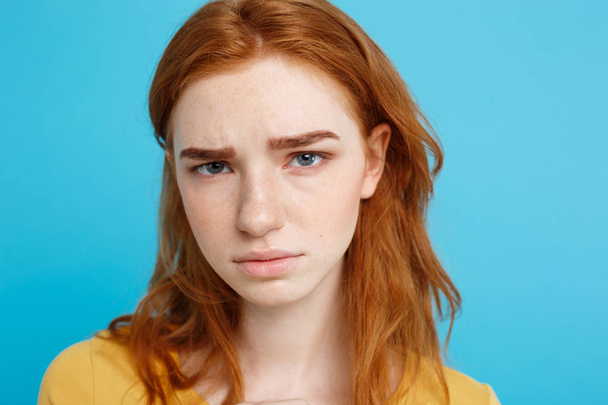 Headshot portret van tedere roodharige tienermeisje met ernstige expressie camera kijken. Kaukasische vrouw model met gember haar poseren binnenshuis. Pastel blauwe achtergrond. Kopiëren van ruimte. - Foto, afbeelding